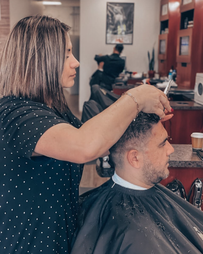 woman giving man a haircut inside barbershop